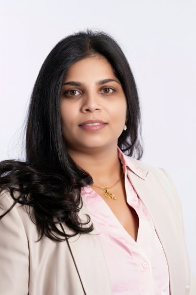A woman with long black hair wearing a light blazer and pink shirt, smiling at the camera.